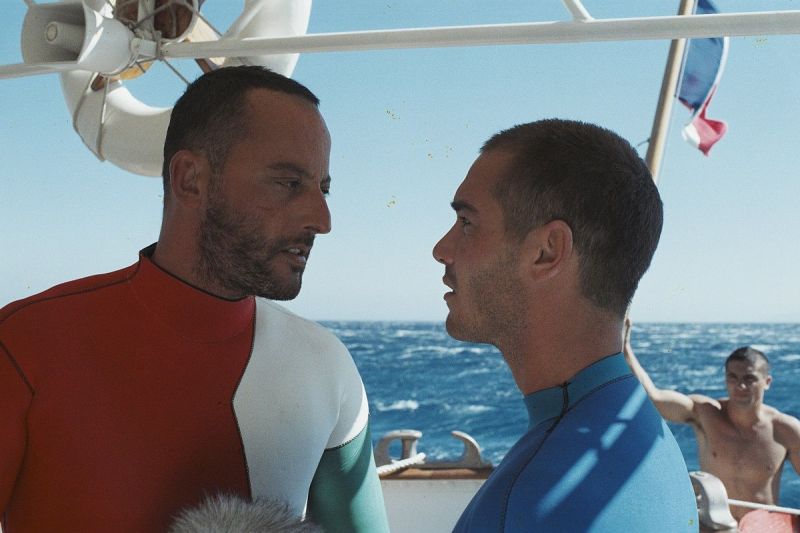 Dwóch mężczyzn ubranych w stroje do nurkowania, w tle morze i niebo.