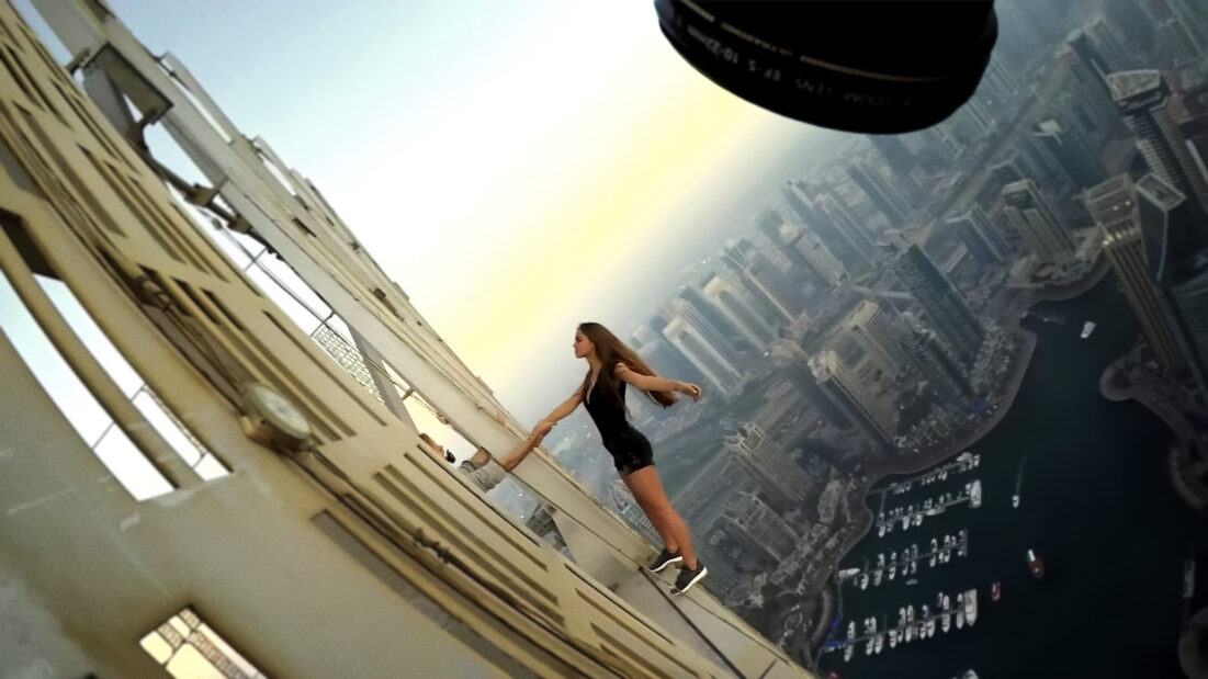 Na zdjęciu kobieta stojąca na parapecie budynku na tle panoramy miasta z wieżowcami w tle.