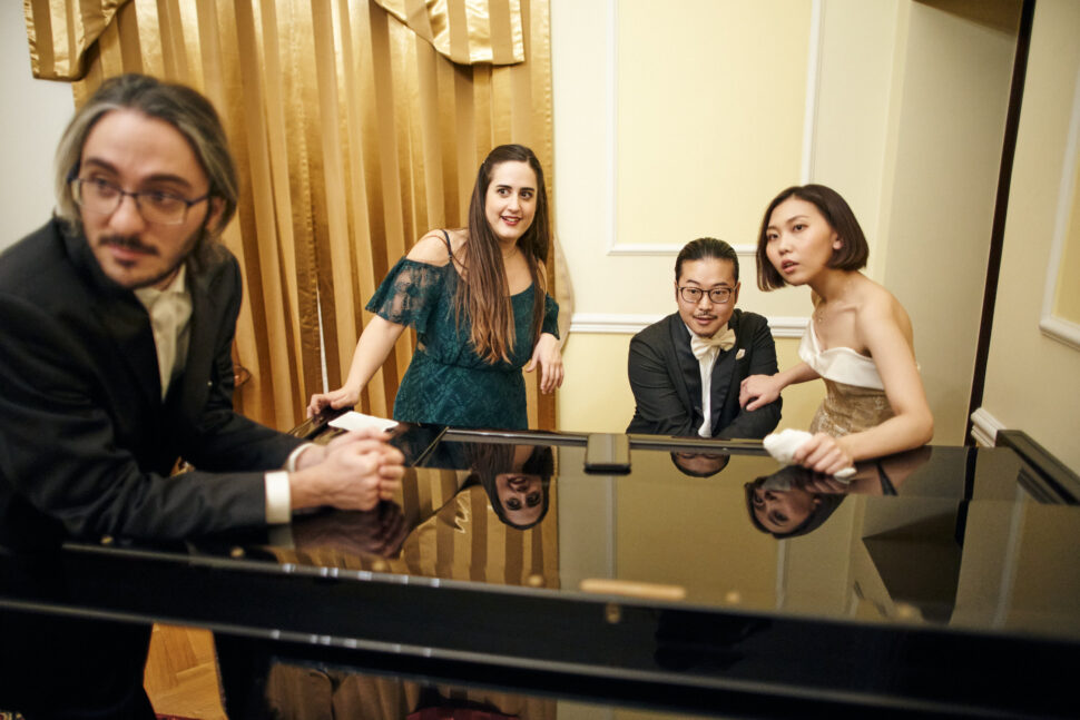Na zdjęciu dwie młode kobiety i dwóch młodych mężczyzn przy fortepianie.