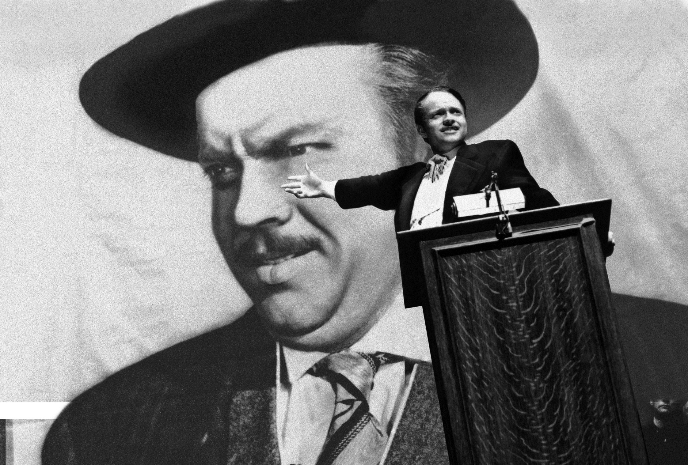 Na zdjęciu mężczyzna przy mównicy przemawiający na tle portretu samego siebie.