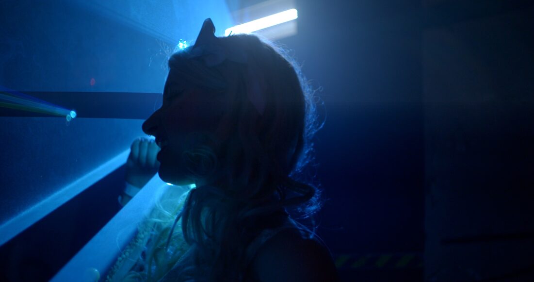 Na zdjęciu ciemny profil kobiecej twarzy na tle granatowo oświetlonego pomieszczenia.